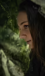 a young woman wearing an open jacket next to bushes