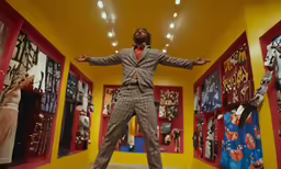a man wearing a suit and tie stands in a room with several other clothes