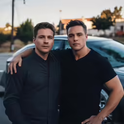 two men leaning up against each other next to a car