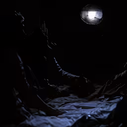 two people sit on the bed in the dark