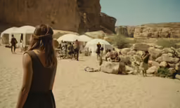 a woman in a black dress walks on the sand toward some tents