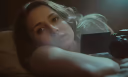 a woman lies on her side with her camera, taking a photo