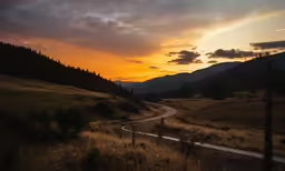 the sun is setting behind the mountains as a road passes by