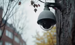 the security camera on this city street light is attached to the side of a building