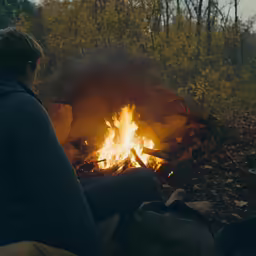 a man sitting by a fire with a cloth draped over it