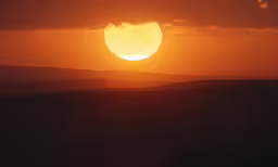 a bright orange sun rises above the mountains