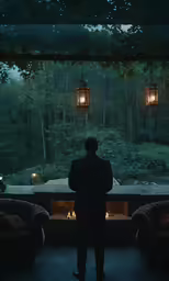 man looking out a window towards a forest filled with lights