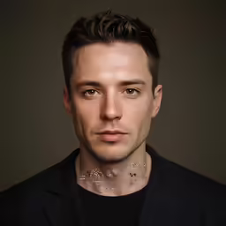 a man with tattoos and collar stands in front of a gray background