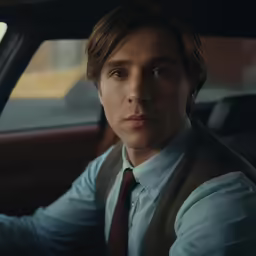 a man in tie and vest sitting inside a car