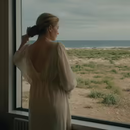 woman looking out window at sand dunes and the ocean