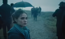 a woman holding an umbrella next to a group of horses