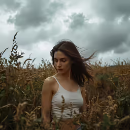 a woman in a white top standing in some tall grass