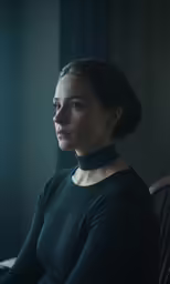 a woman in black sitting at a desk wearing a black choker