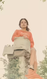 a girl wearing an orange sweater sitting on top of a stone pillar