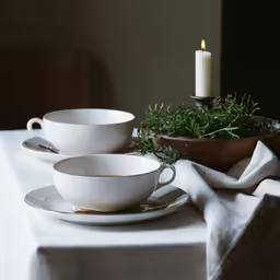 white dishes on table with candle next to bowl and candle holder