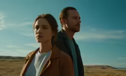 a man and woman standing close together with the sky behind them