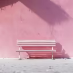 a white park bench is against a pink stucco wall