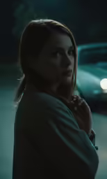 a woman standing outside in front of a car at night