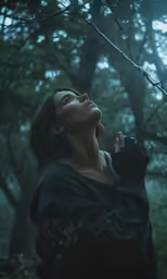 woman looking up while standing in a forest