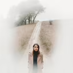 woman with long hair wearing a trench coat standing on a trail