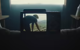 man bent down looking into television screen with mountains in background