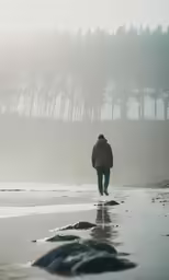 man walking down beach with trees in background