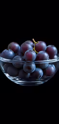 a bowl filled with grapes sitting on top of a black surface