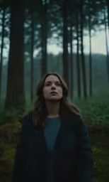 a woman stands among the tall pines in the woods