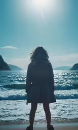 a woman stands on the beach as she looks out at the water