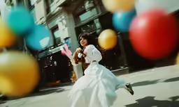 a woman in a long white dress is chasing colorful balloons