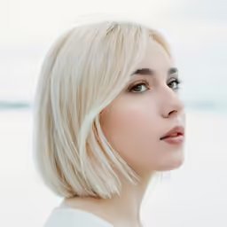 a blonde woman standing in front of the ocean with her head turned to look straight ahead