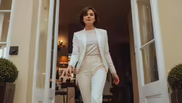 a woman in white suit walking through a doorway