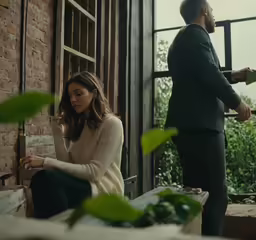 a man stands next to a girl, reading and standing near some windows