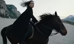 woman riding a horse on the beach in front of a rocky mountain