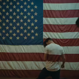 man in white shirt holding a baseball bat in front of an american flag
