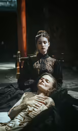 two girls in period clothing laying down with one holding the other