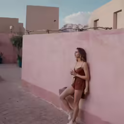 a woman in brown shorts leaning against pink wall