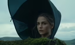 a woman holding a black umbrella standing in the middle of a mountain