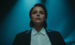 a woman with a serious look standing in front of some bright lights