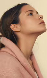 a woman wearing a light pink sweater looks up with her head tilted to the left