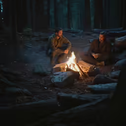 two men sitting around a camp fire in the woods