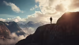 man on top of mountain with clouds and sunlight coming through
