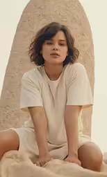 a woman sitting on a sandy surface wearing white