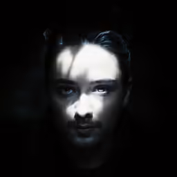 the man is in darkness looking up at the camera