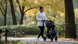 a woman in a white coat and sneakers walking with a baby in a stroller