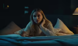 a young woman laying in bed talking on her phone