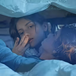 two people laying in bed with one woman touching her face