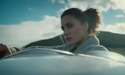 a girl looking at the camera and looking into the distance with mountains in the background