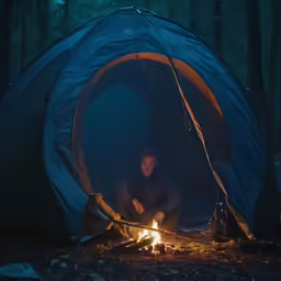 a man sitting in a tent in the woods at night