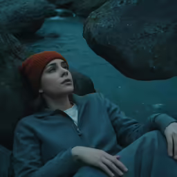 a woman sitting on rocks near water and looking off into the distance